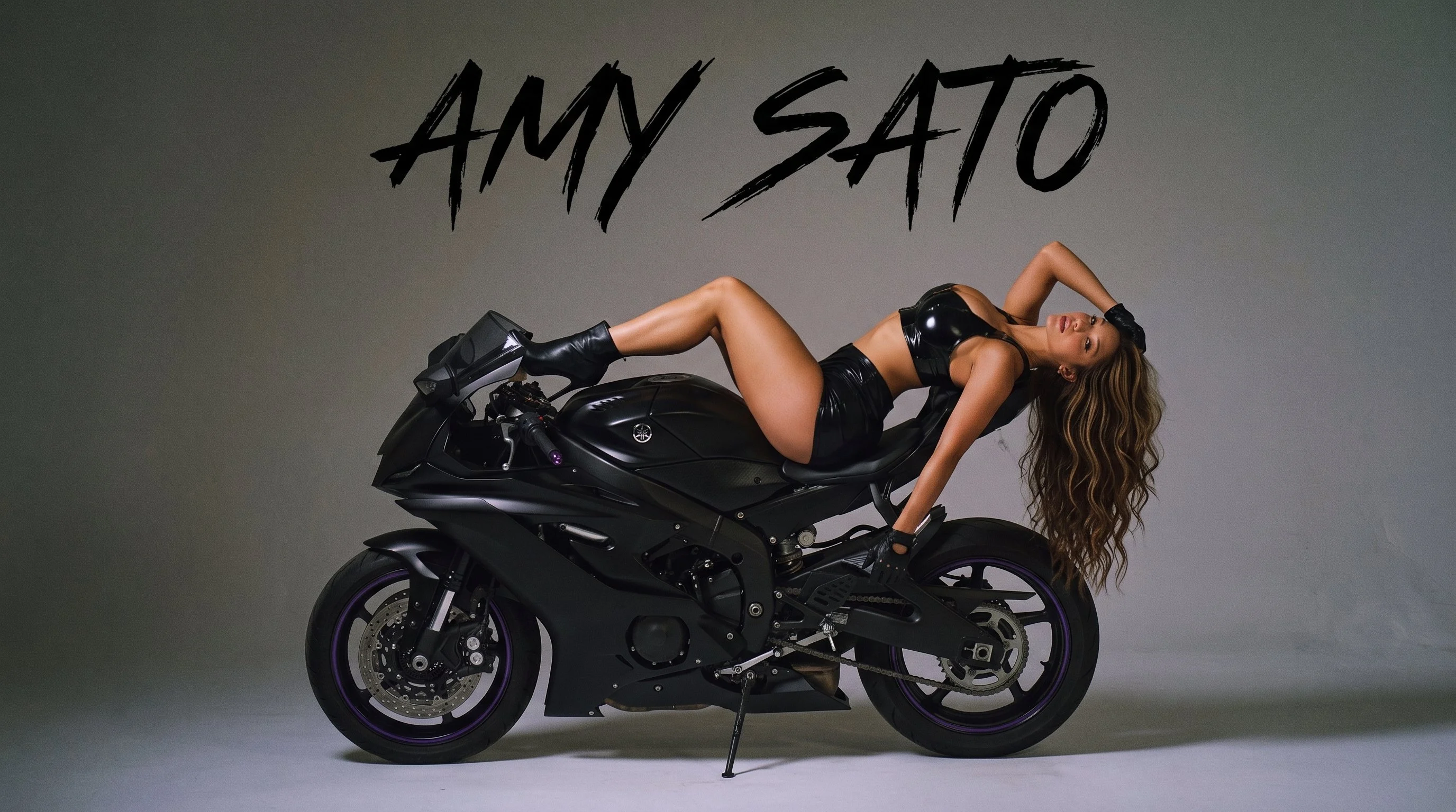 Amy Sato reclining on a black motorcycle, with AMY SATO lettering above
